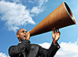 Man holding a large megaphone to his mouth with sky background.