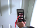 photo: hand holding manometer pressure gauge in front of closed door