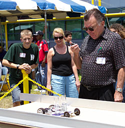 photo of man holding stop watch and looking at Hydrogen Sprint car, while young man and woman watch too