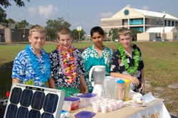 Photo of students wearing hawaiin shirts and leis show off their solar slushy machine.