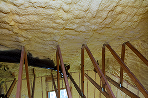 Photo of attic space with spray foam insulation on roof deck, looking from attic  down through trusses and to first floor with insulated walls.
